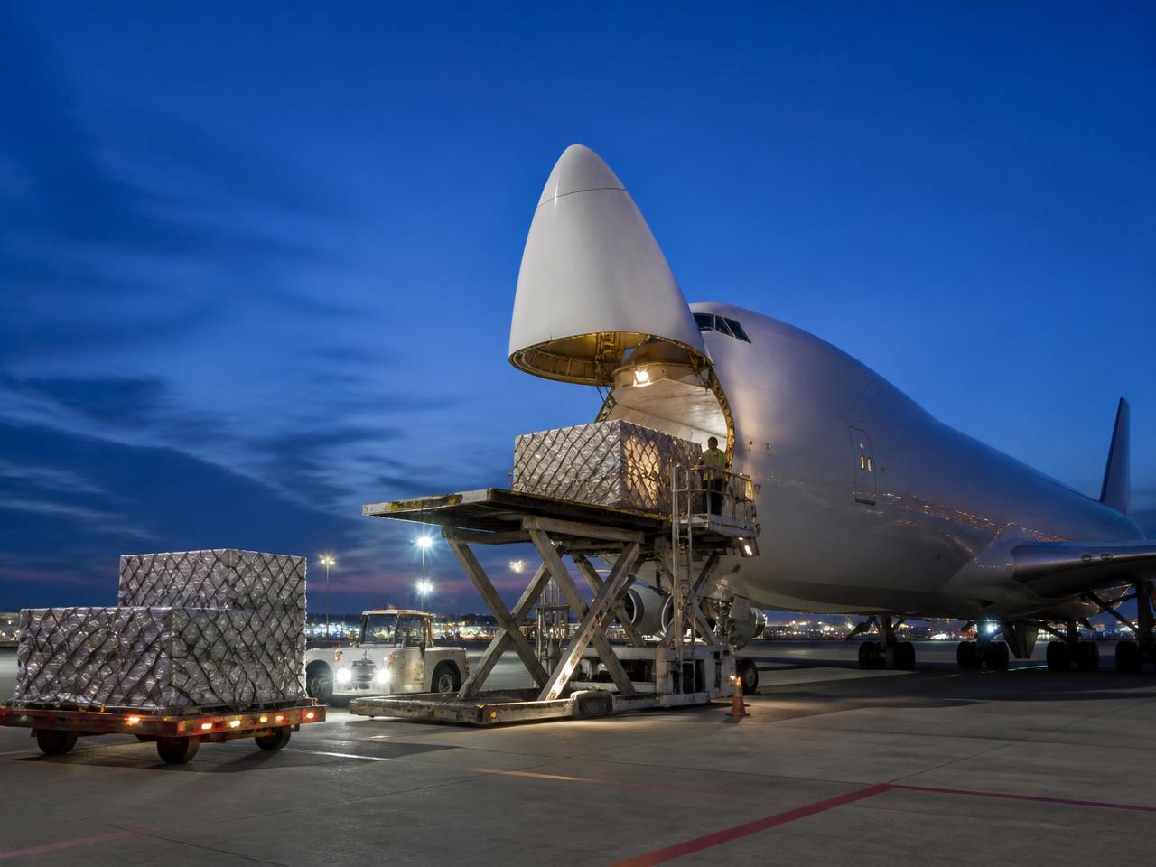 Air cargo pallets being loaded into a freighter aircraft at dusk